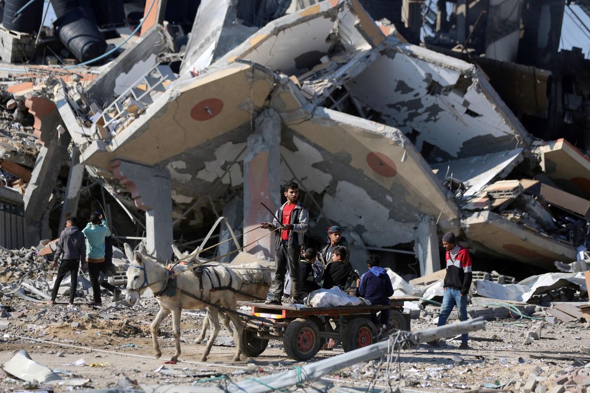 Überall Zerstörung: Menschen fahren im Flüchtlingscamp Al-Maghazi mit einem Eselwagen an eingestürzten Gebäuden vorbei (16. Januar 2024). 